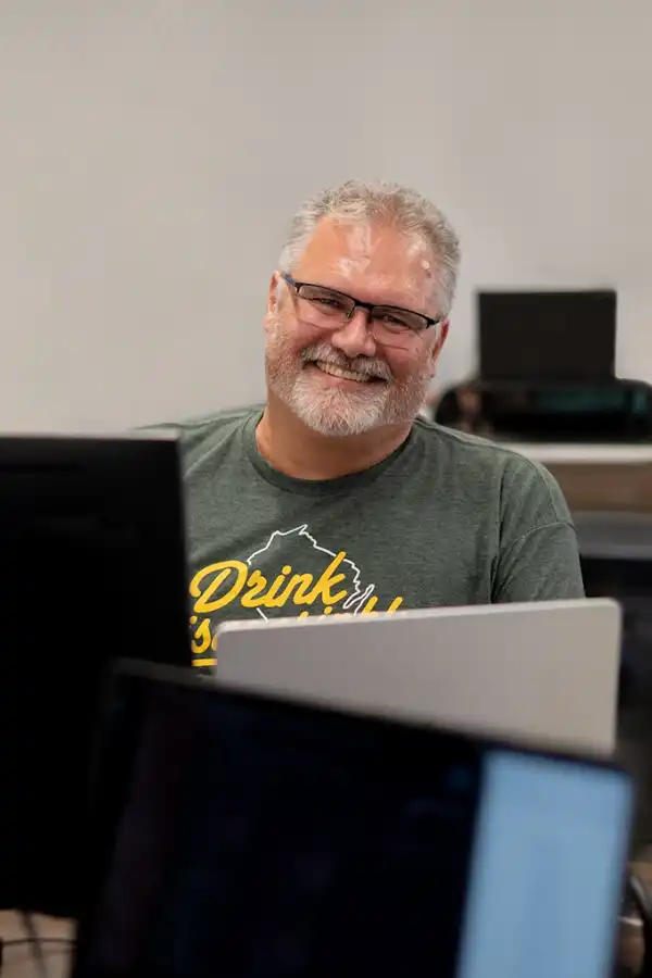 A man with a majestic beard sitting behind a laptop and smiling at the camera.