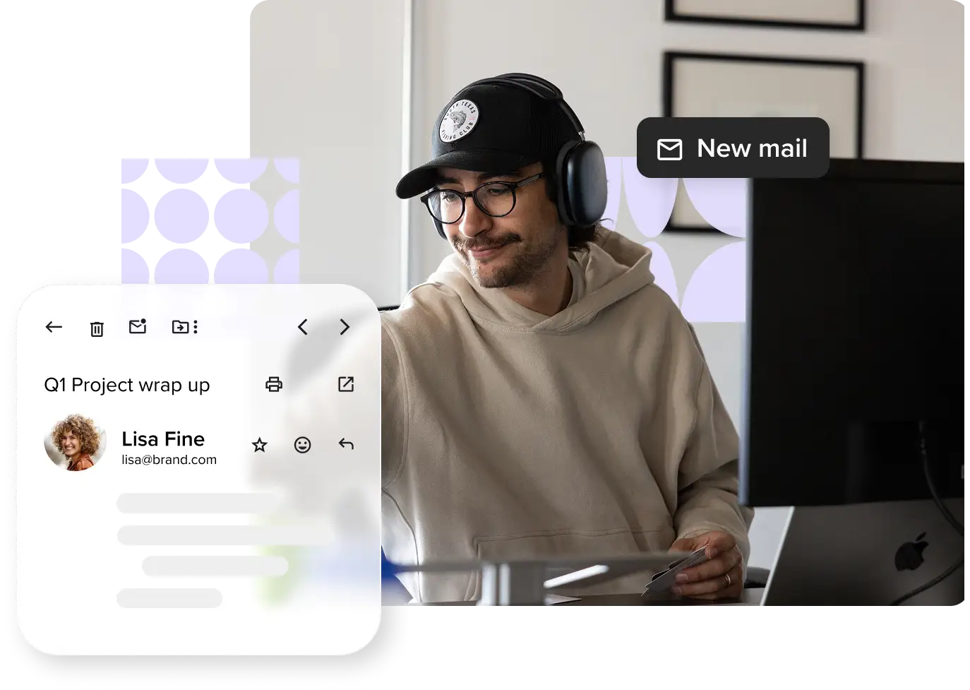 A man wearing a hat, headphones, and glasses smiles while looking down at his desk