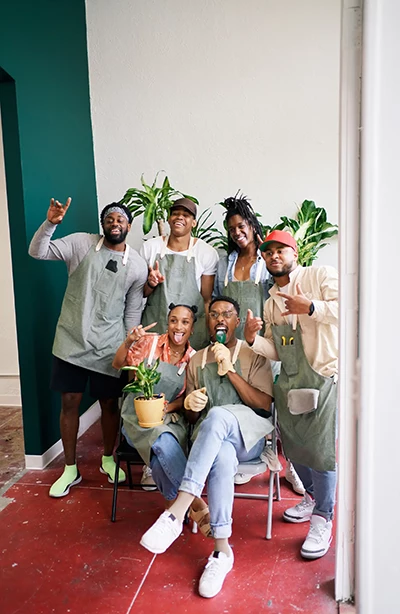 Small group of people pose together wearing aprons and holding potted plants.