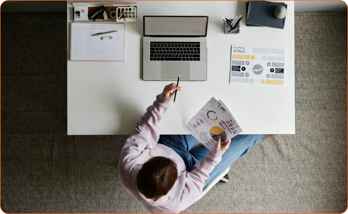 Man sits at computer desk looking at printed graphs and charts in front of computer