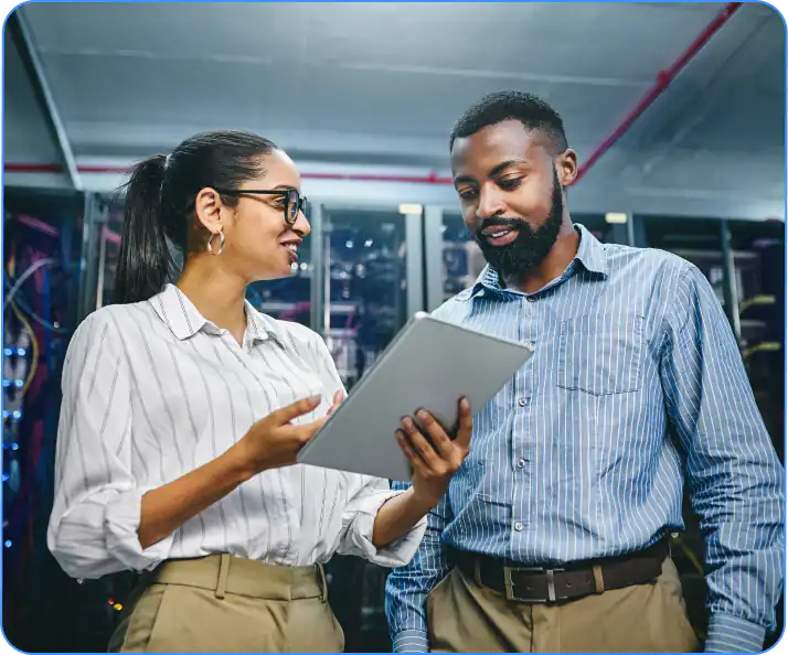 Man and woman standing in server room smiling at tablet