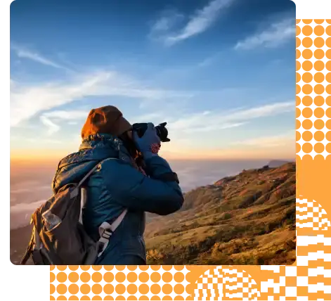 Creative male photographer wearing a blue puffer and a backpack while capturing a sunset in the mountains