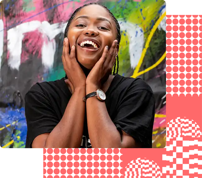 A happy artist with braided hair smiles widely, holding their hands to their cheeks. They are standing in front of a colorful, abstract graffiti background, wearing a black T-shirt and a wristwatch.