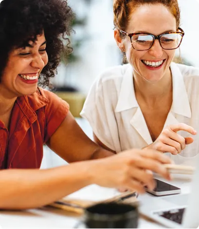 Two women smiling and pointing at computer screen reflected in glasses